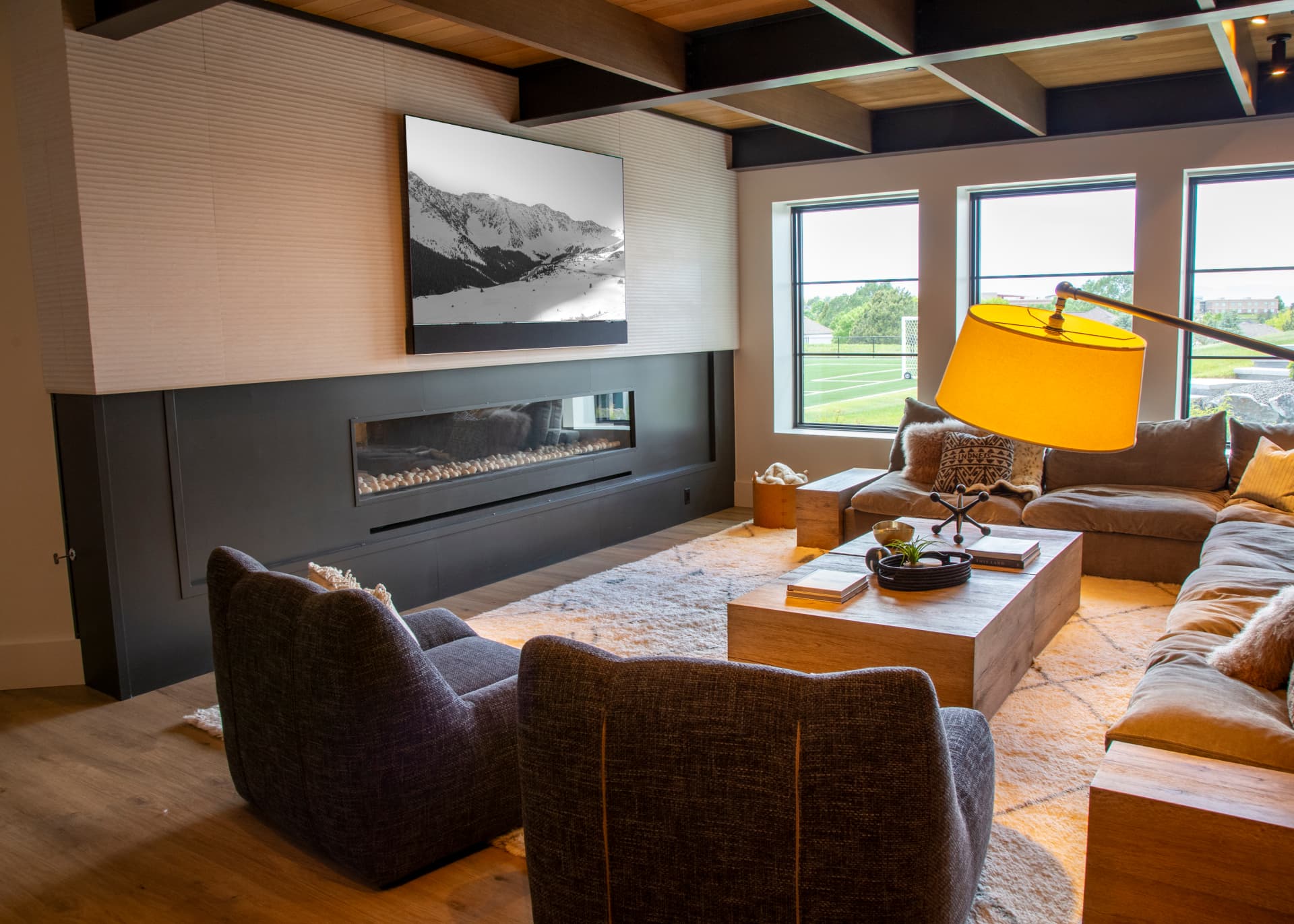 Lower-level rec room with large television above a linear fireplace and lounge seating
