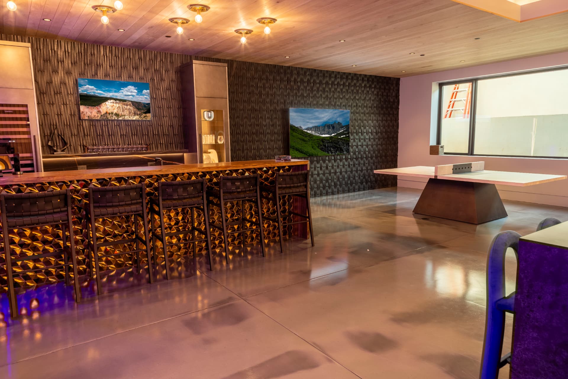 Lower-level bar and game room with multiple wall-mounted displays and warm accent lighting